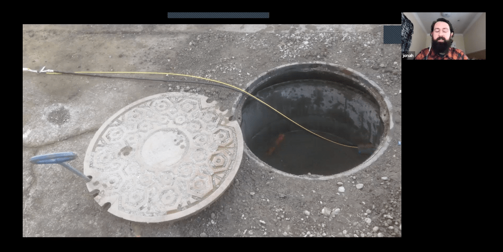 Screenshot from a video showing a manhole cover with a fiber strand coming out of it onto the street.