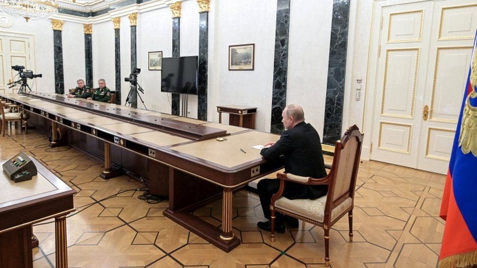 Photograph of Putin sitting at a giant table with two people all the way down at the other end.