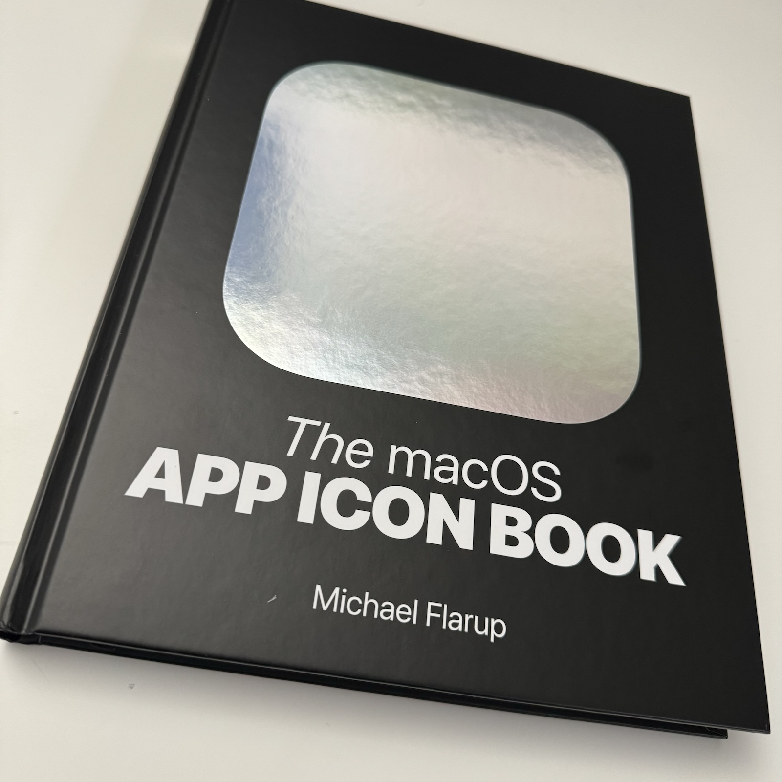 Photograph of the cover of the “The macOS App Icon Book” which is black, hardbound, and has a iOS-shaped silver foil embossing on the front.